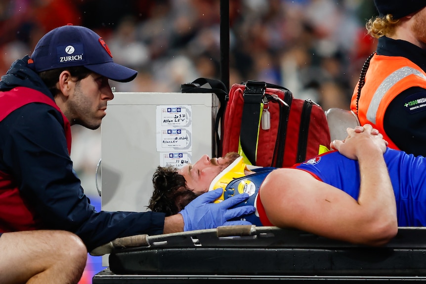 Angus Brayshaw is lying on a stretcher with a neck brace on and his eyes closed