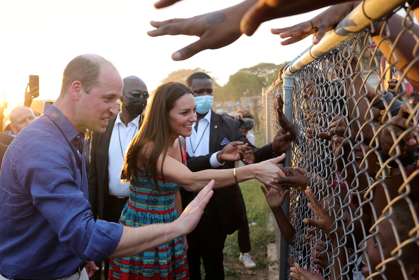 William and Kate grasp the hands of black children through a chicken wire fence.