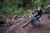 A mountain biker rides on a curved muddy bush track.