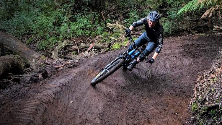 A mountain biker rides on a curved muddy bush track.
