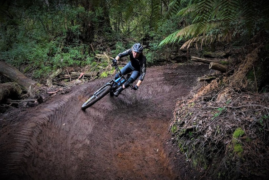 A mountain biker rides on a curved muddy bush track.
