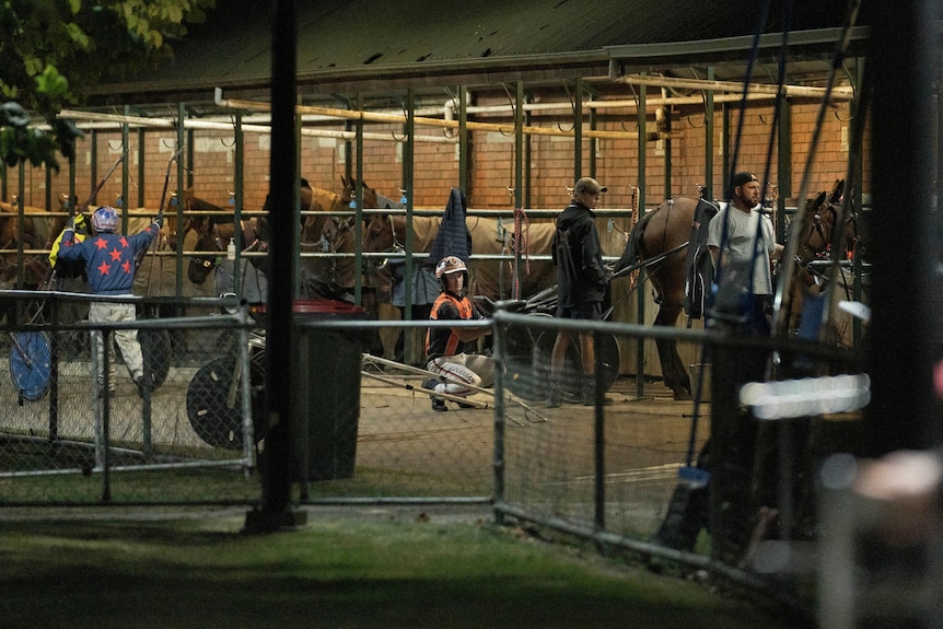People work at a stables at night.