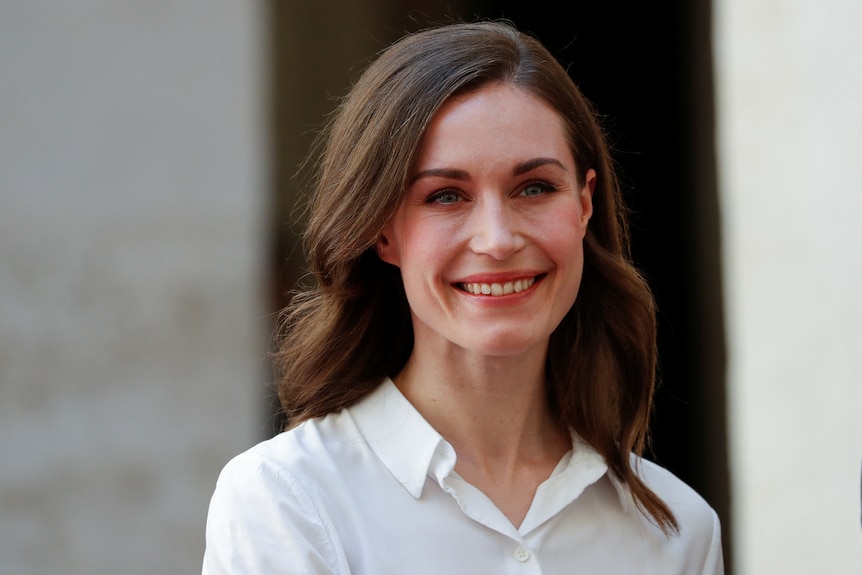 Sanna Marin smiles widely as she stands outdoors in a white collared shirt