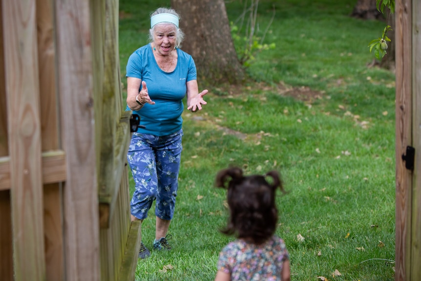 An old woman smiles at a child as she walks through an open gate 