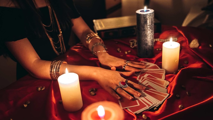 a pair of bejewelled hands is spreading out a deck of tarot cards at a lamp-lit table