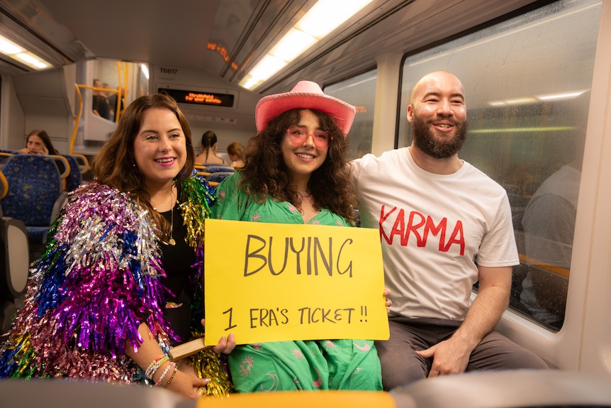 three people on a train holding a sign that reads buying one eras ticket