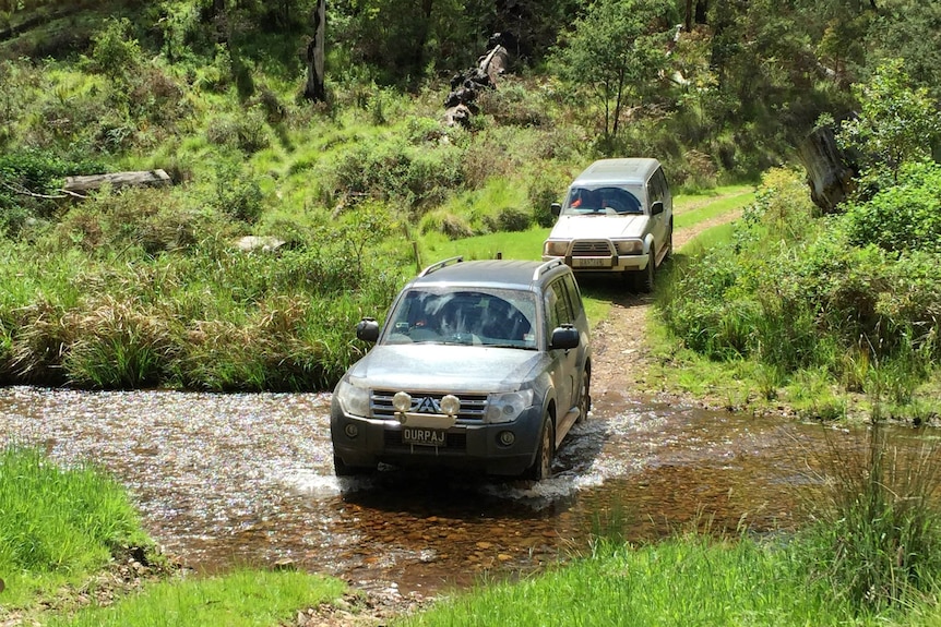 Two four-wheel-drives go through a creek crossing