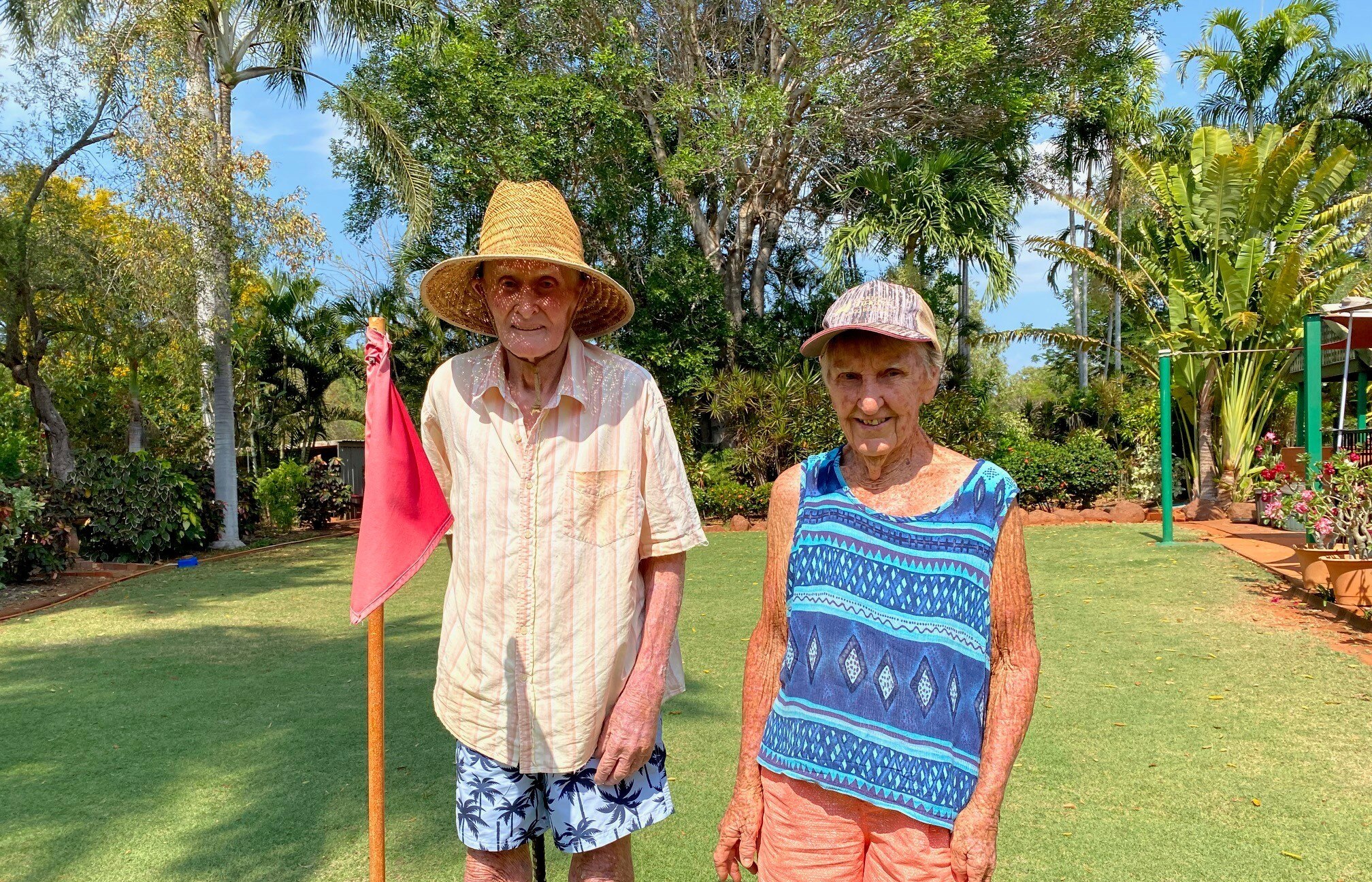 A couple smile in the sunshine on a lawn with a red gold flag
