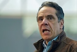 New York Governor Andrew Cuomo with his mouth open looking right and up while wearing a jacket over a blue shirt