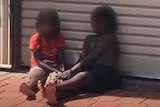 Two children sitting barefoot on a brick driveway