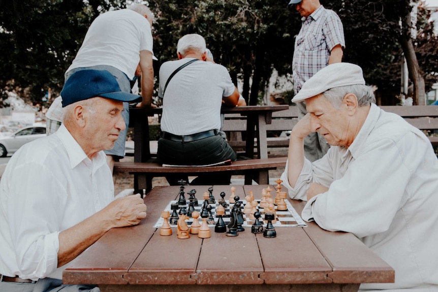 Two old men play chess outdoors