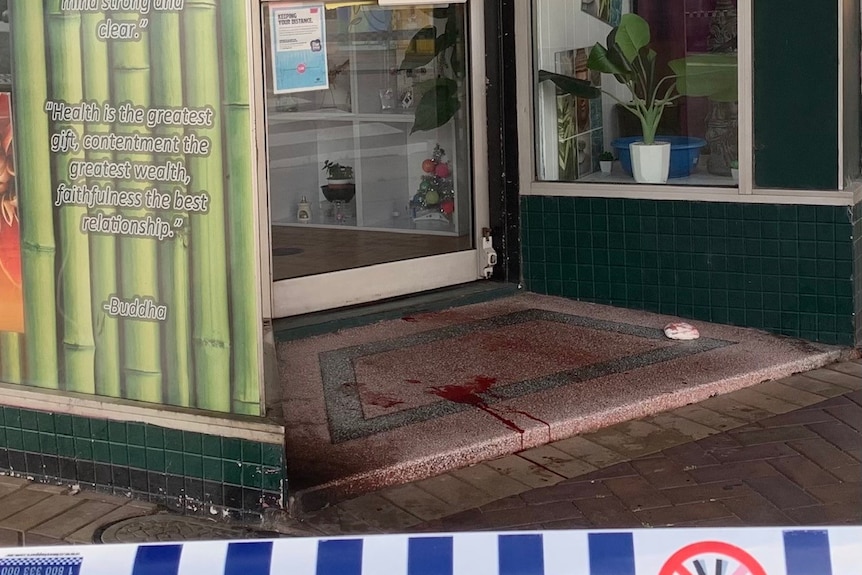 A cafe facade cordoned off with police tape. Blood is pooling at the door.