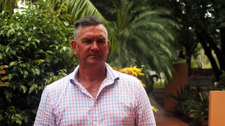 David McGinlay stands by palm trees wearing a checked chirt