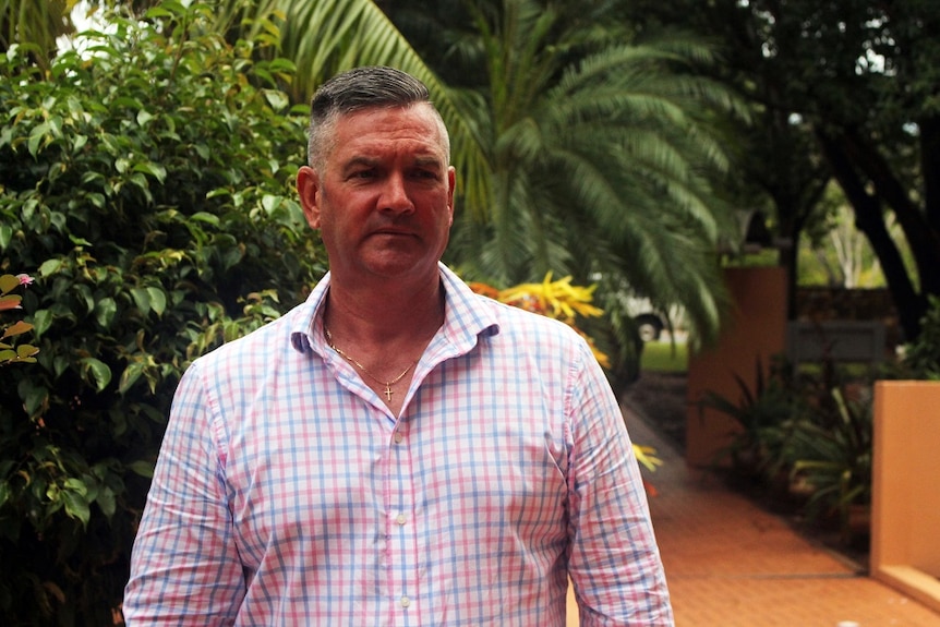 David McGinlay stands by palm trees wearing a checked chirt