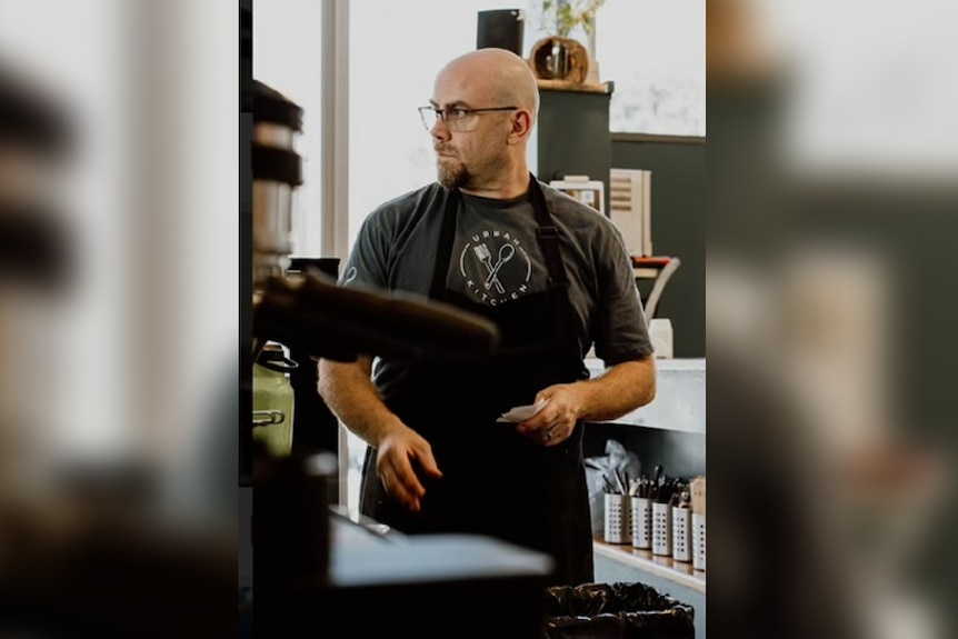 A bald man standing behind a coffee machine whose name is Paul Watters.