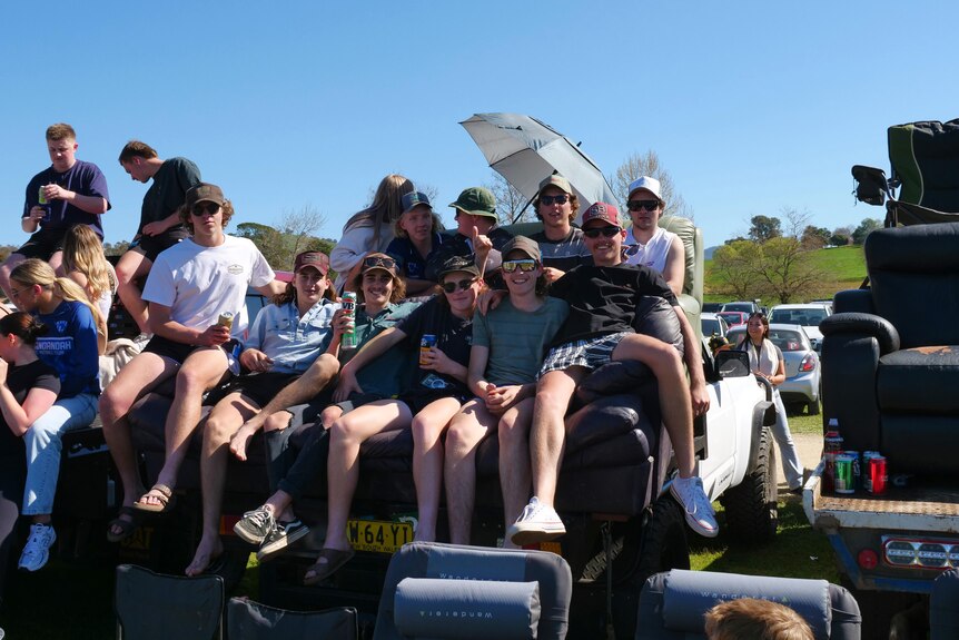 A group watches football sitting on ouches in the back of a ute.