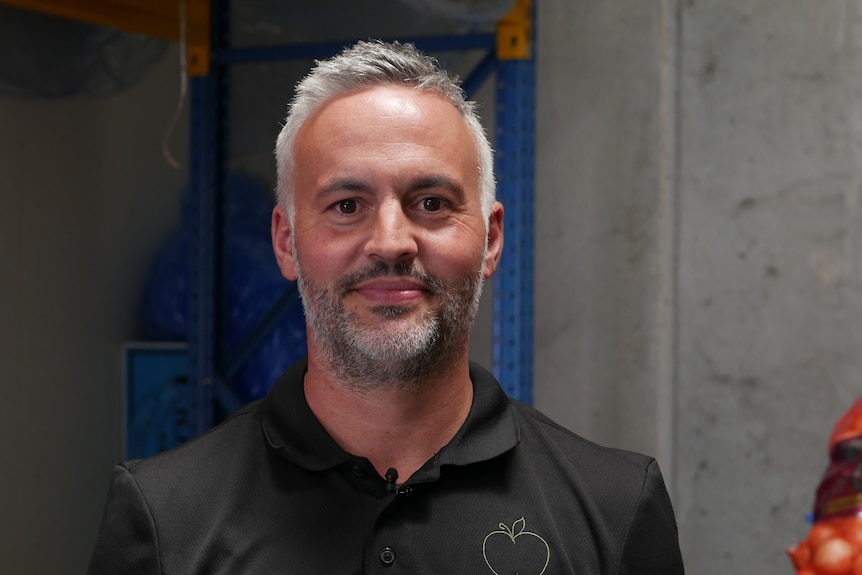 a man with short grey hair and a black polo fills the centre of the frame