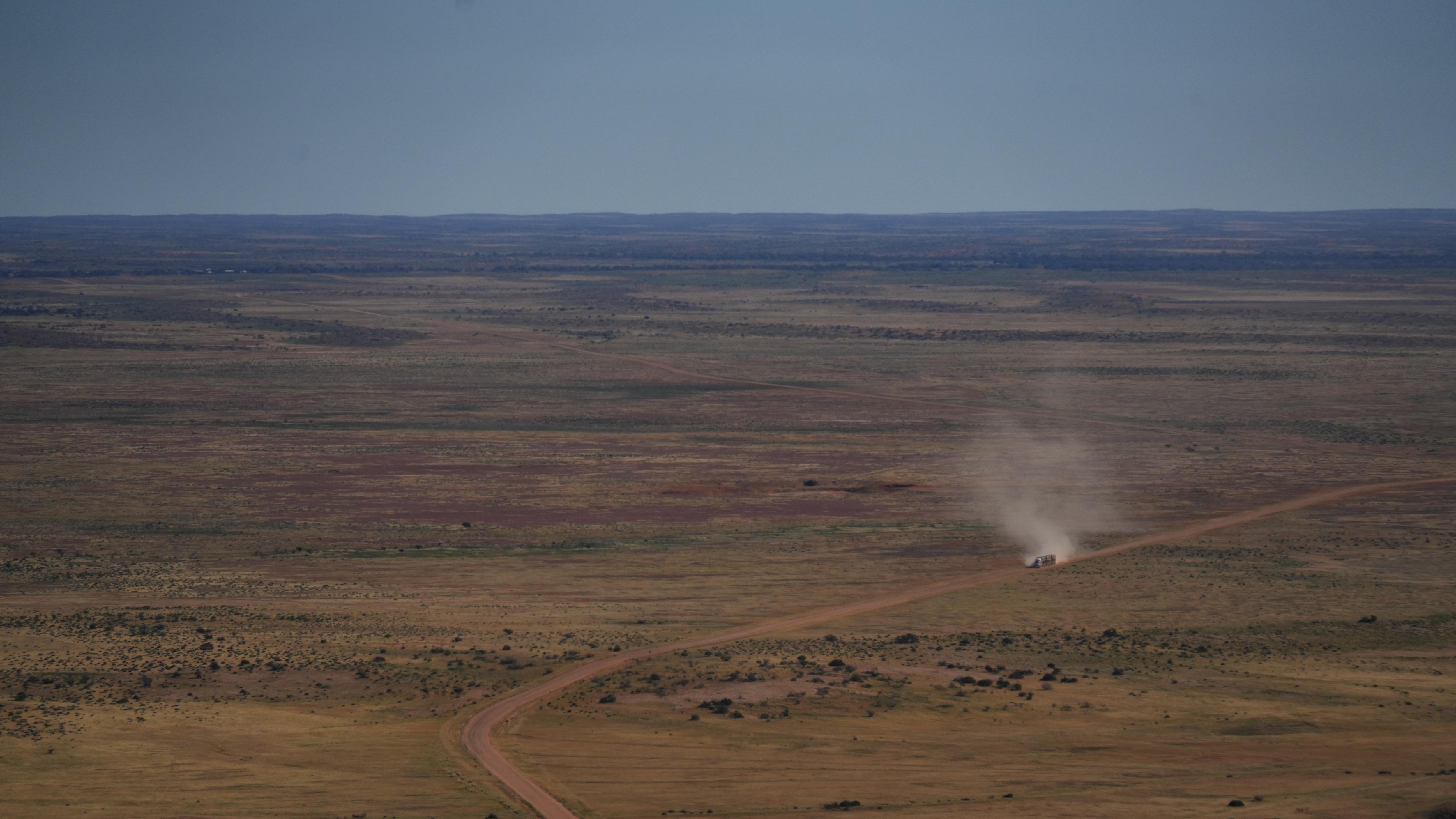Taken from a plane, a wide flat landscape with a dirt road through the middle, and a truck driving along