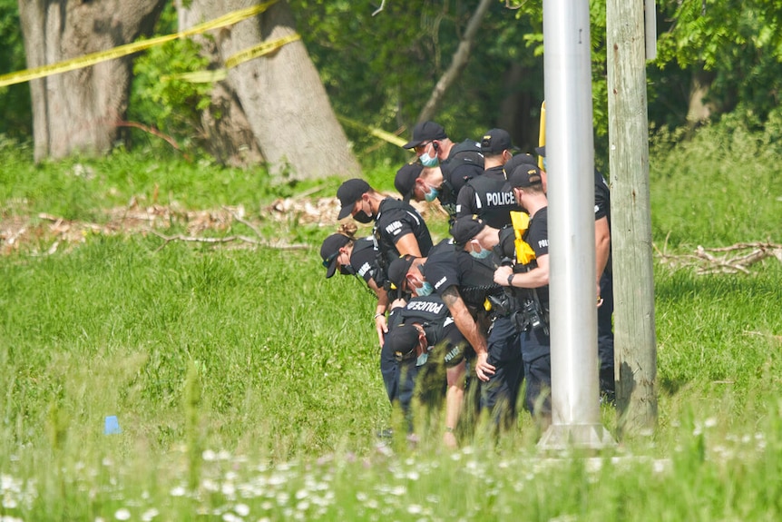 A line of police officers look for evidence at the scene of a car crash in London.