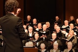 A conductor wearing a black suit standing in front of a choir.