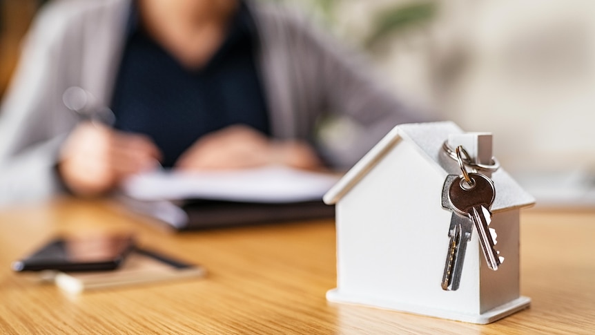 A home buyer looks at documents. In the foreground of the image is a model house and keys.