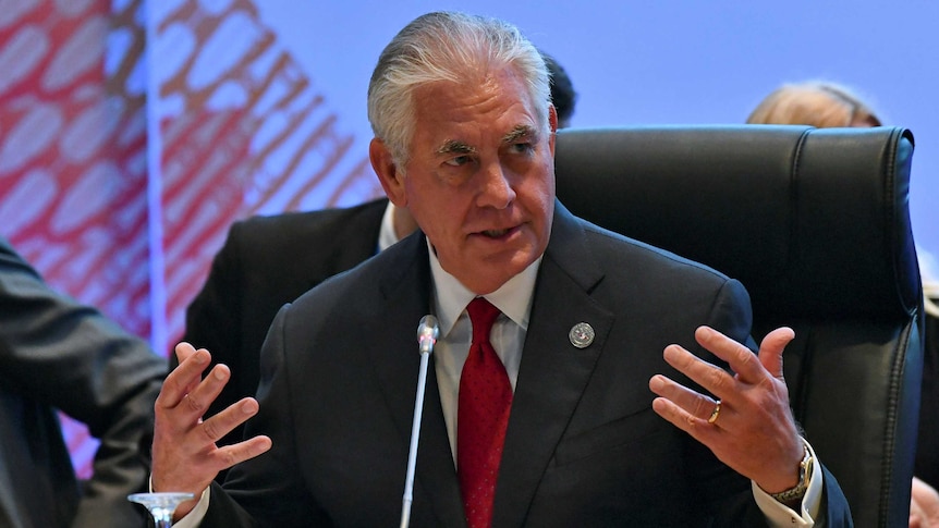 Rex Tillerson gestures at a meeting while wearing a suit with a red tie.