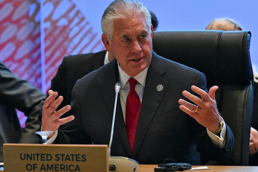 Rex Tillerson gestures at a meeting while wearing a suit with a red tie.