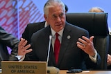 Rex Tillerson gestures at a meeting while wearing a suit with a red tie.