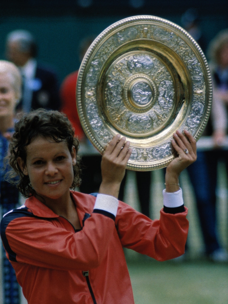 A female tennis player holds up a silver plate trophy after winning an important match