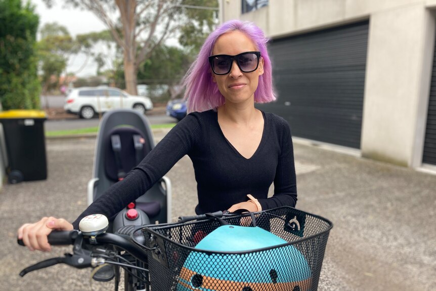 A woman with purple hair standing next to a bike looking at the camera