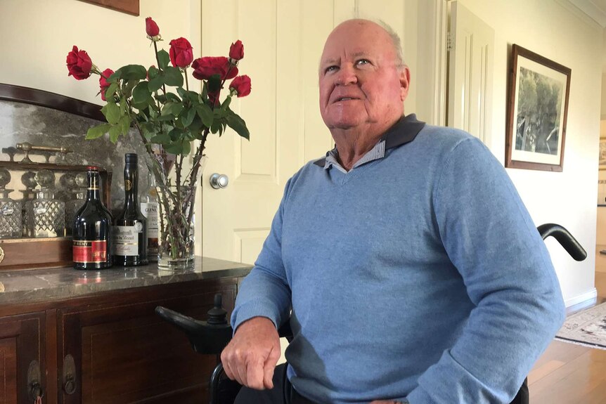 Former MP Graham Edwards pictured at home in his wheelchair next to a sideboard with a vase of red roses.