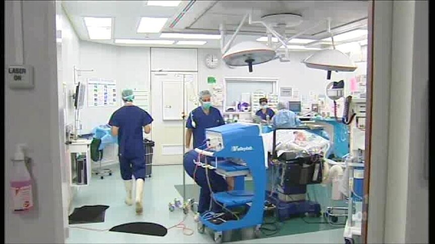 Several hospital staff in blue surgical scrubs working in an operating room