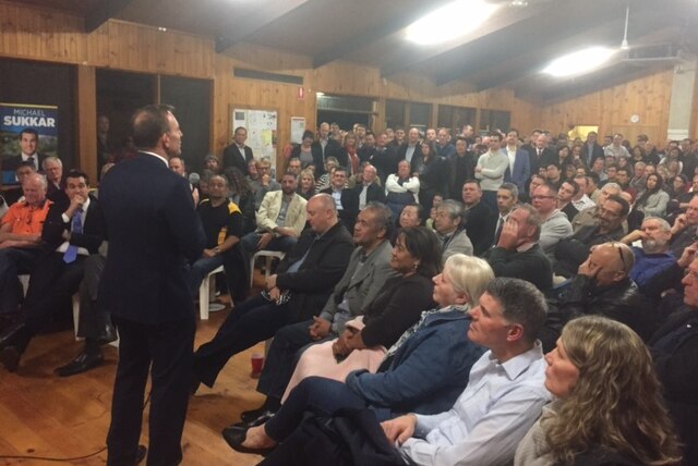Tony Abbott stands in front of a room of supporters. His back is to the camera.
