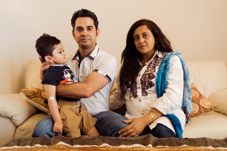Qasim Butt holds his son Shaffan, while sitting on a couch next to his wife Mehwish.