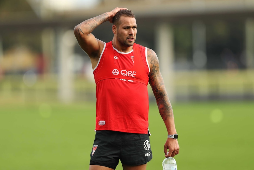 A Sydney Swans AFL player stands with a hand on his head at a training session.