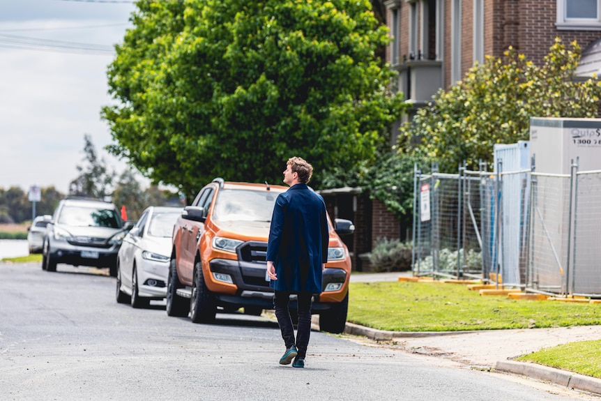 A man walks down a street lined with a few trees and a construction site.