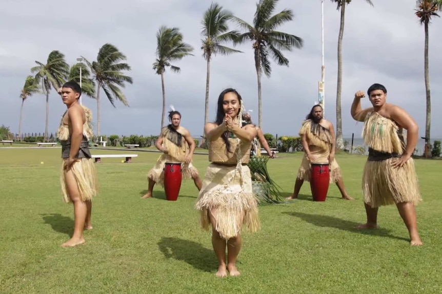 People in traditional Fijian attire perform a dance in front of palm trees near the beach.