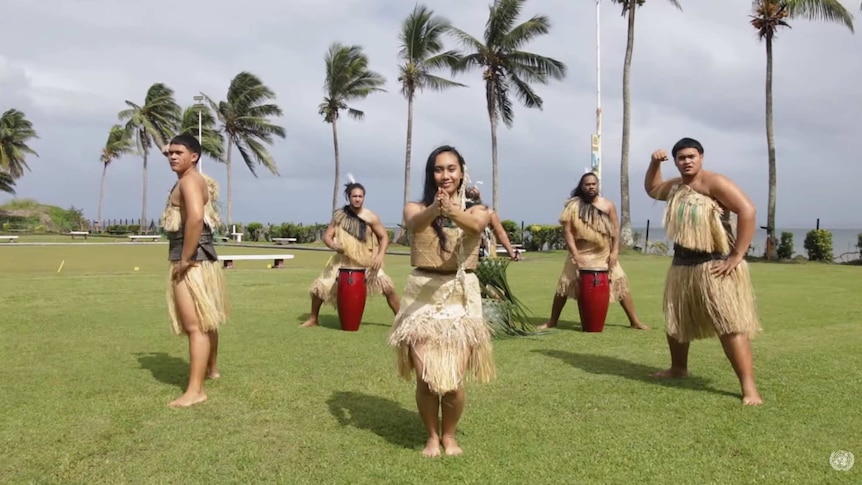 People in traditional Fijian attire perform a dance in front of palm trees near the beach.