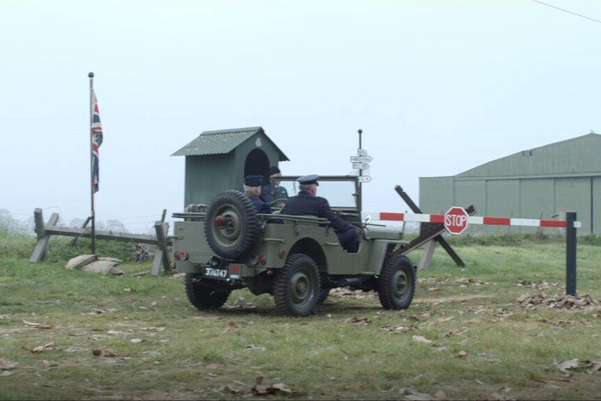 A military car approaches a world WWII-era gate in a field