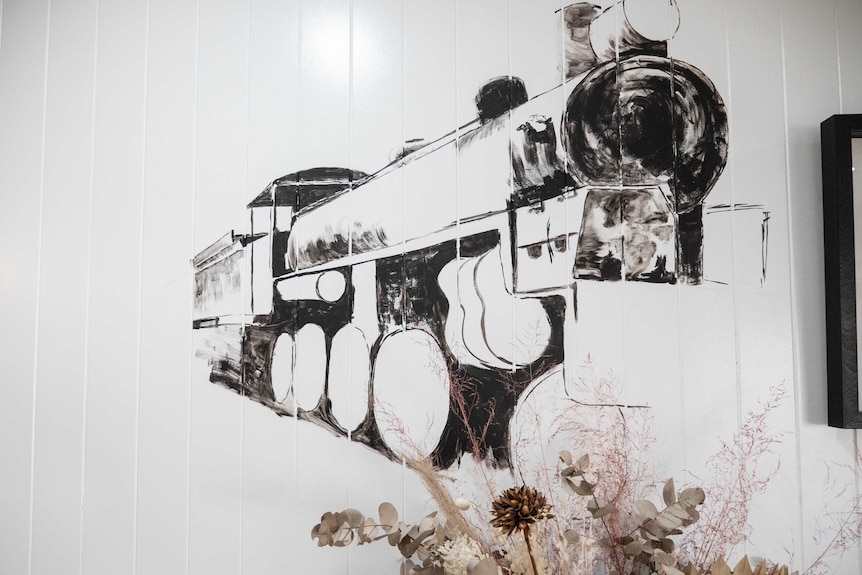 A black and white painting of a 3D train on a white wall. Native flowers are below it.