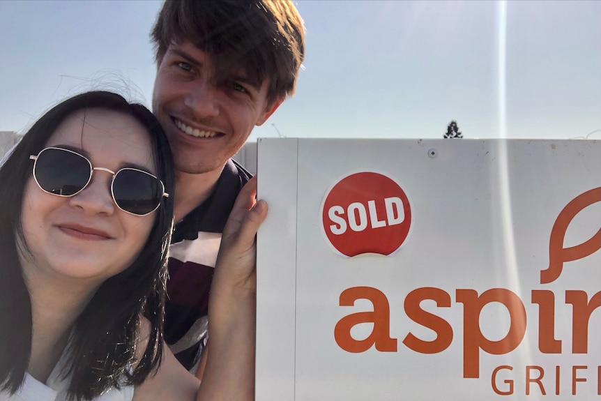 A man and woman smiling next to a sold sign.