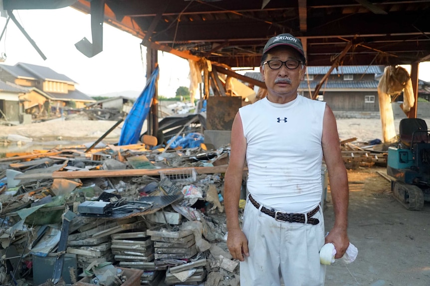 Soji Ono poses for a photo with piles of rubbish and debris behind him.