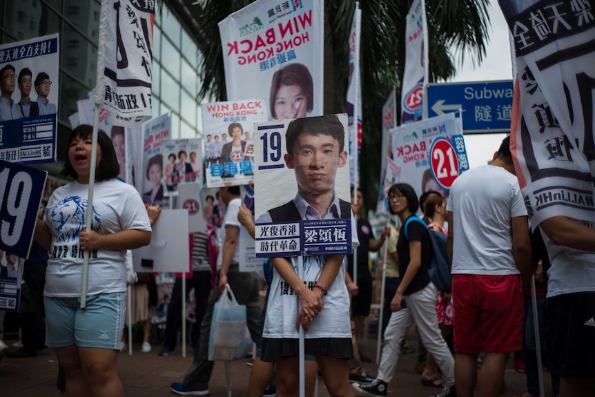 A campaigner stands behind a placard of candidate Baggio Leung.