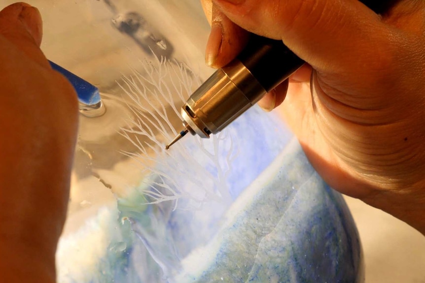 A hand engraving trees onto glass