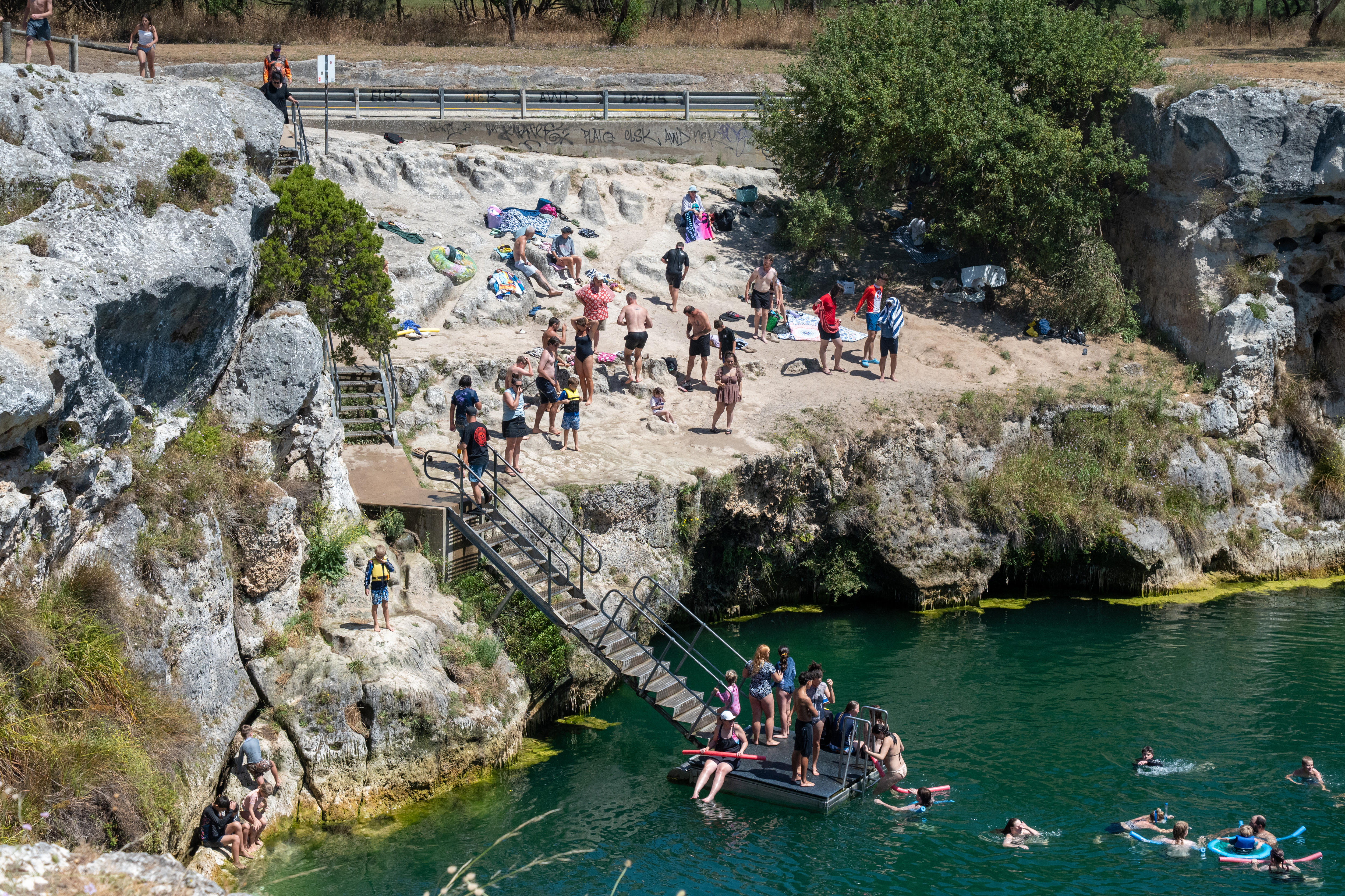 Escaleras que bajan desde los acantilados a un lago de agua, con flotadores en el agua y en la parte superior de las escaleras.