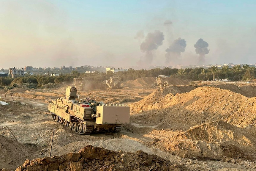 a tank rolling through piles of dirt as clouds of smoke rise in the background
