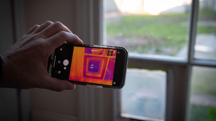 A hand holds a phone on its side, with the screen open on a camera app that shows red and purple shapes