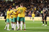 A group of soccer players wearing yellow and green hug each other during a game