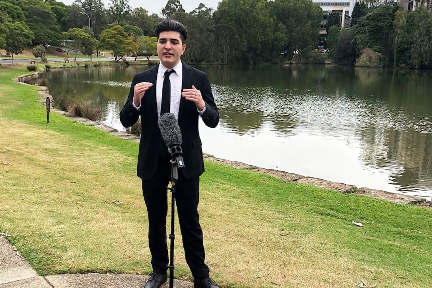 UQ student Drew Pavlou speaks into a microphone beside the UQ Lakes at the St Lucia campus in Brisbane.