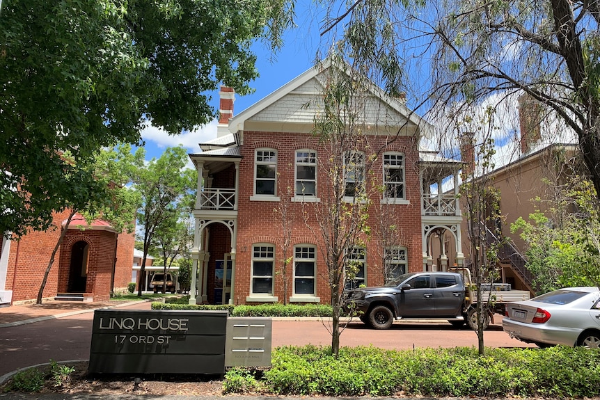 An old red brick building with trees in the foreground. 